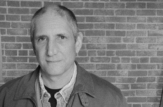 A black and white photo of voice actor Stephen Russell against a brick wall.