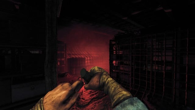 Amnesia The Bunker: the player pulls the pin on a grenade while a red glow shines ahead of them.