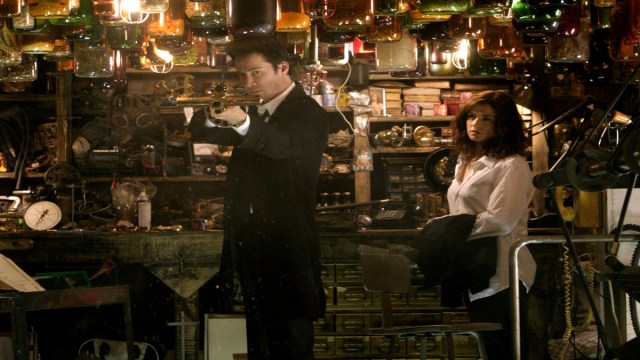 John Constantine (Keanu Reeves) tries out a gun while Angela Dodson (Rachel Weisz) looks on.