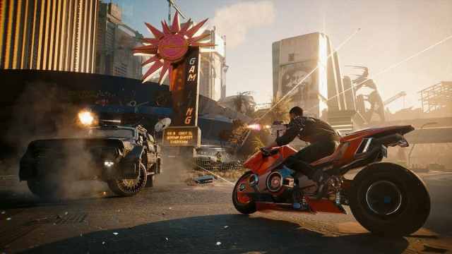 Cyberpunk 2077: someone on a red motorcycle shooting at an armored car.