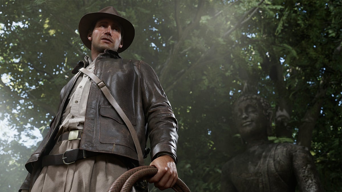 Indiana Jones and the Great Circle: the titular Indiana stands proud in a jungle, holding his whip, with a statue behind him.